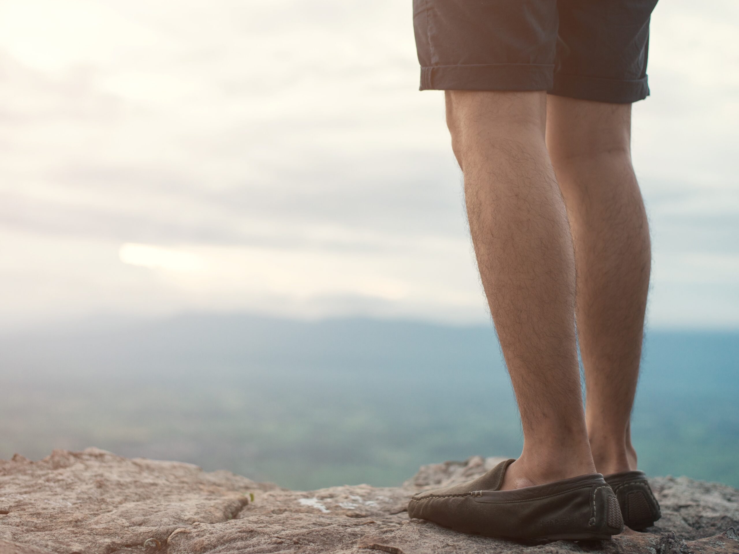 a man standing at the top of a cliff peering out into the clouds.